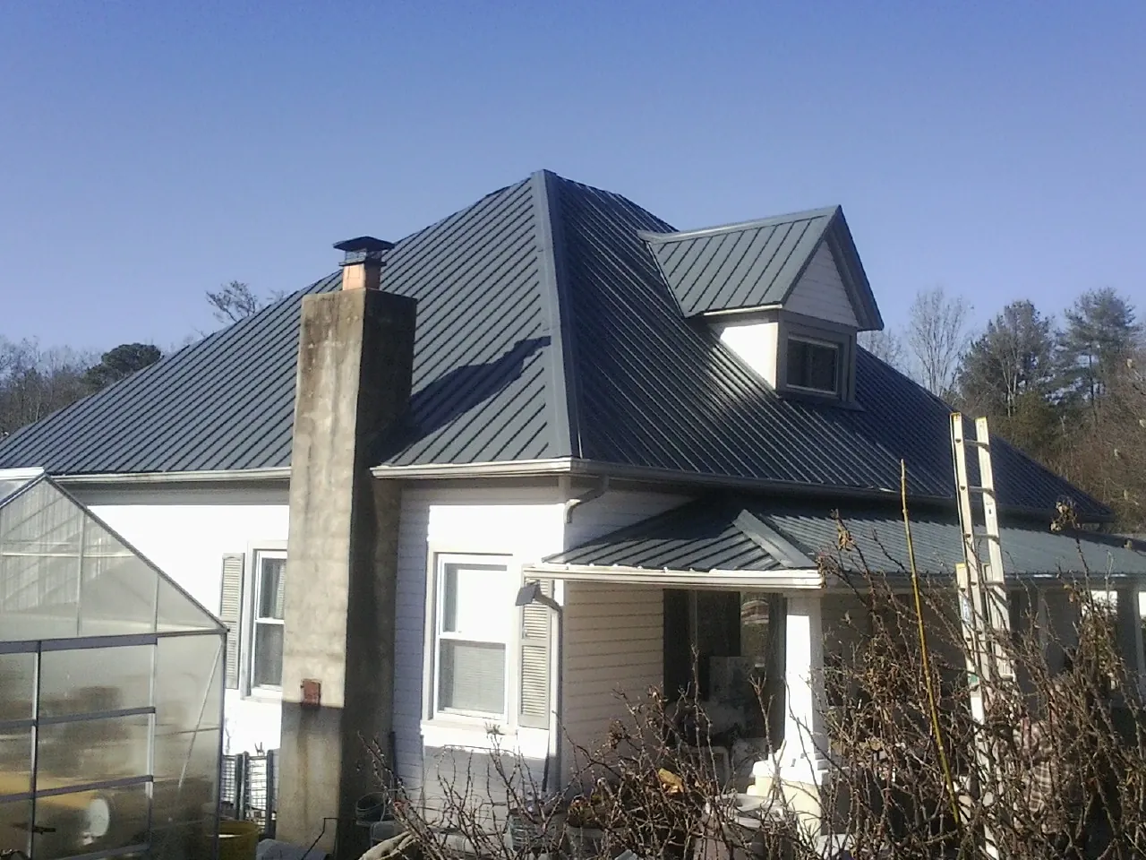 Dark blue standing seam metal roof on a white farmhouse with dormer — Slate & Tile Roof Repair by Roofing Brothers in Tidewater