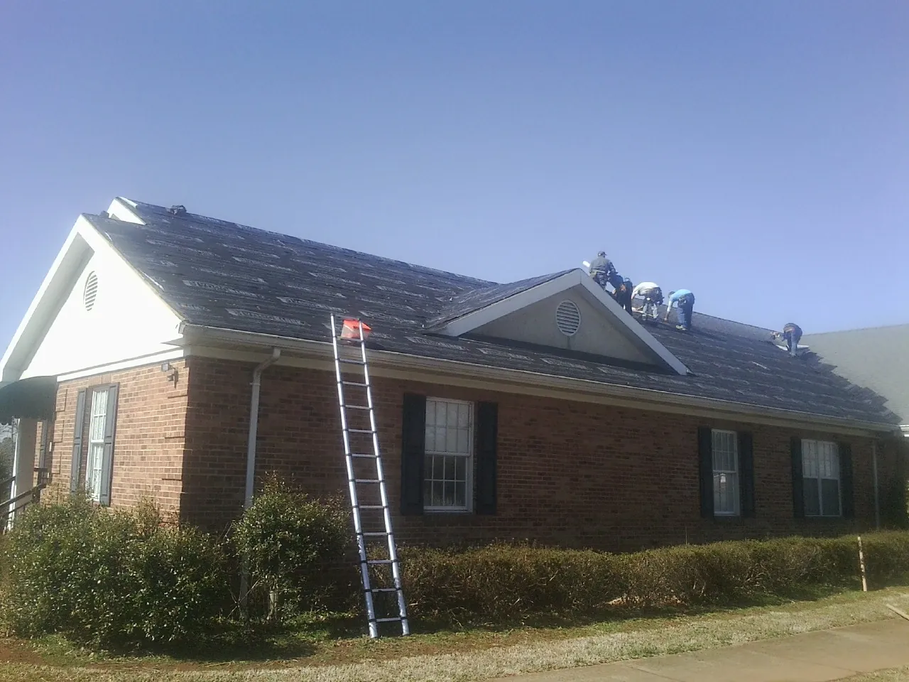 Crew tearing shingles off a brick ranch roof with a ladder set — Metal Roof Repair work by our crew in Tidewater