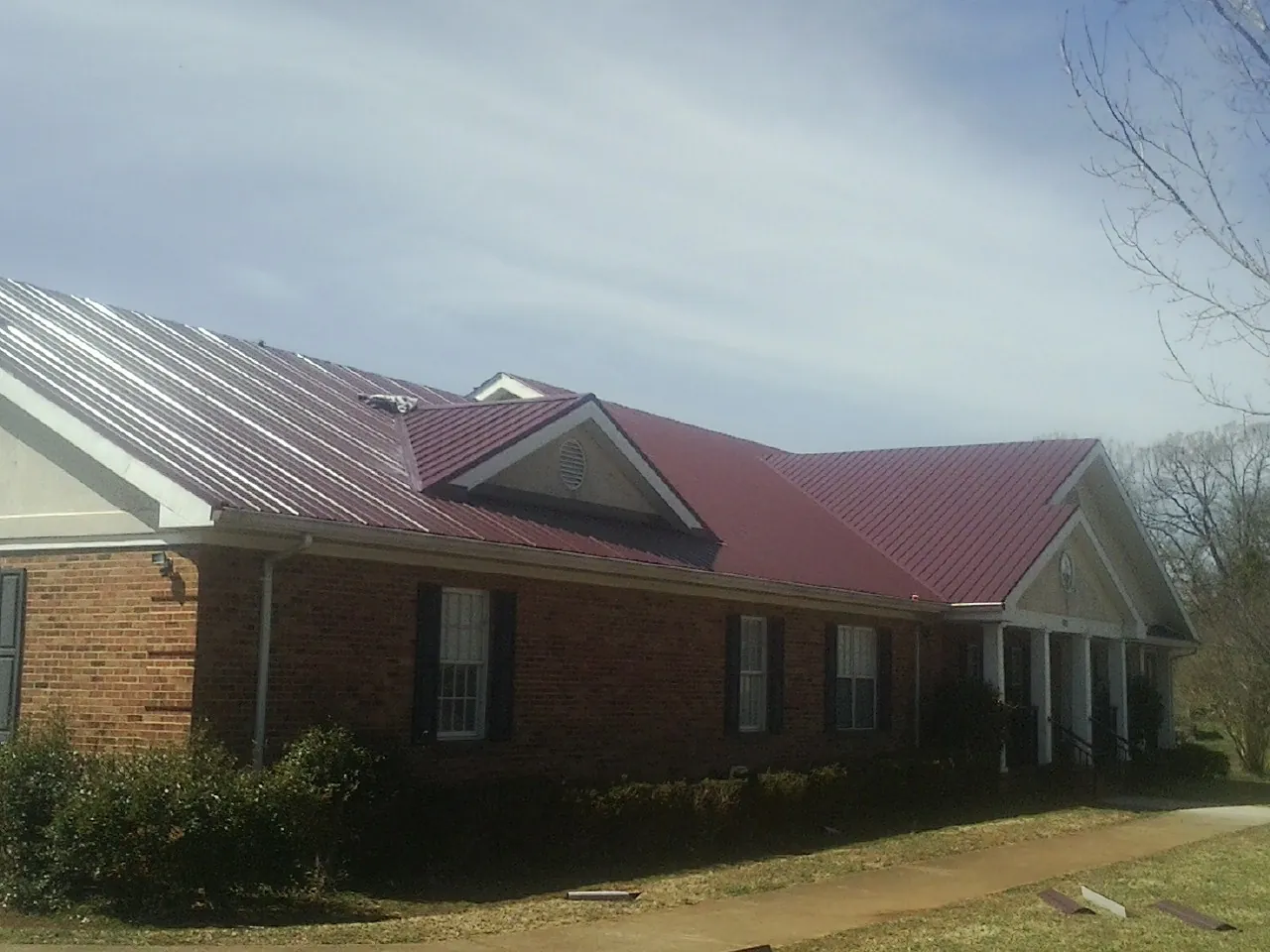 Red metal roof with gabled entries on a long brick building, from a Hail Damage Roof Repair job in Tidewater