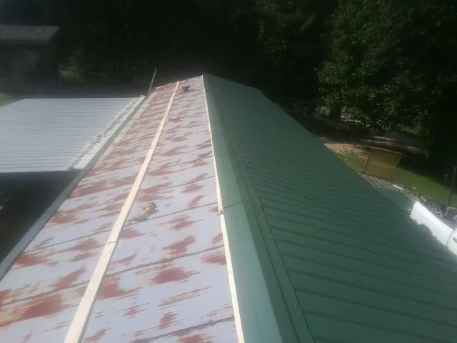 Old rusted panels beside newly installed green metal roofing — Wind Damage Roof Repair by Roofing Brothers in Tidewater