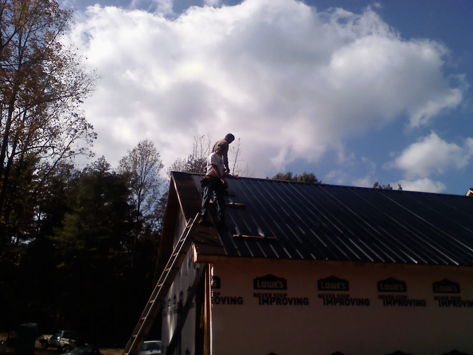 Roofer fastening dark metal panels high against a cloudy sky, from a Roof Inspection job in Tidewater
