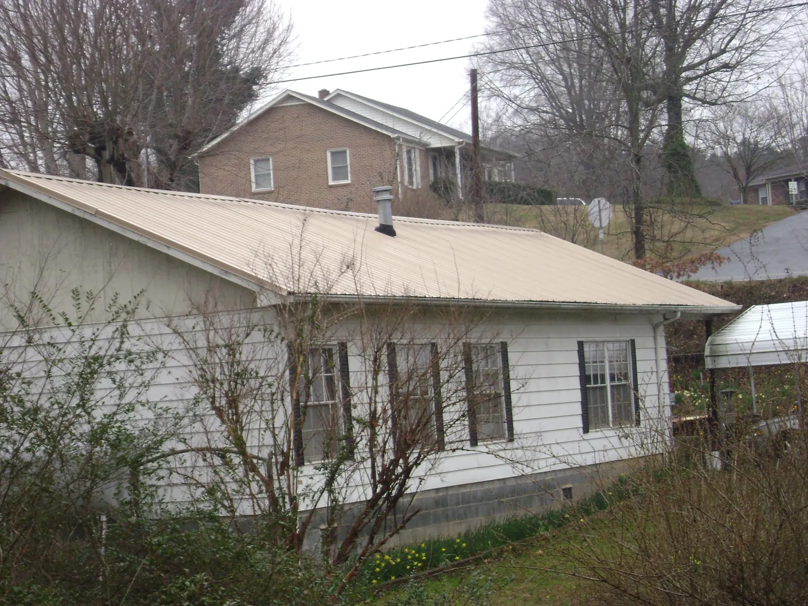 Tan metal roof on a white sided house set into a hillside — Commercial Roofing by Roofing Brothers in Tidewater